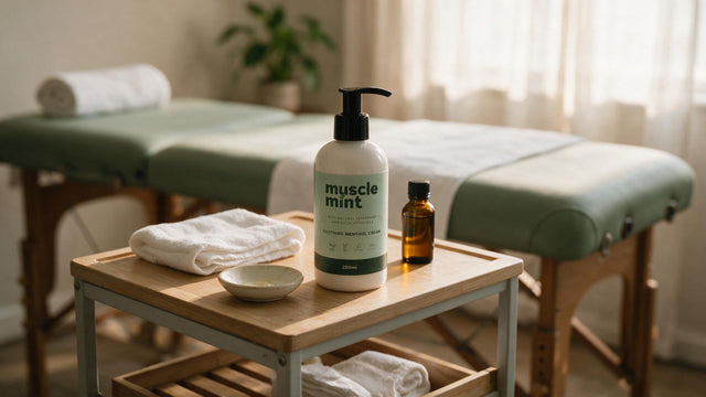 Muscle Mint 250ml bottle on a massage therapist's trolley beside folded towels and a small dish of oil