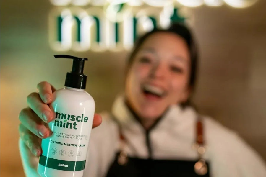 Zolene Mayberry, founder of Muscle Mint, smiling and holding out a 250ml bottle of Muscle Mint Soothing Menthol Cream