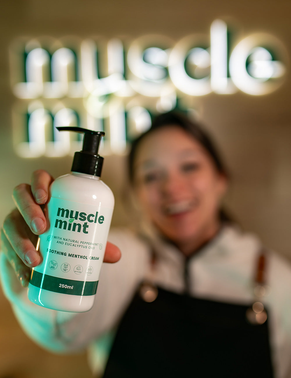 Person holding a 'muscle mint' bottle with a blurred background featuring the brand name.