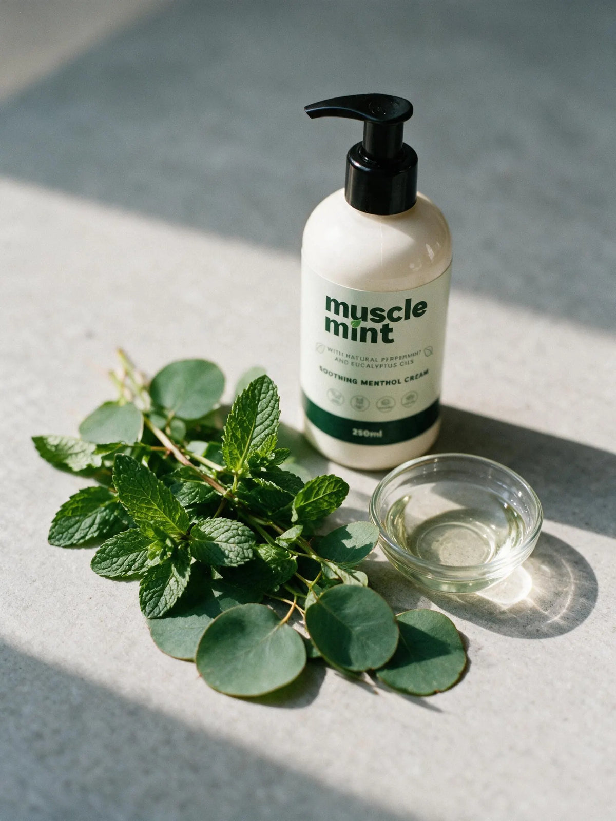 Fresh peppermint sprigs and eucalyptus leaves beside a small dish of oil and the Muscle Mint 250ml bottle