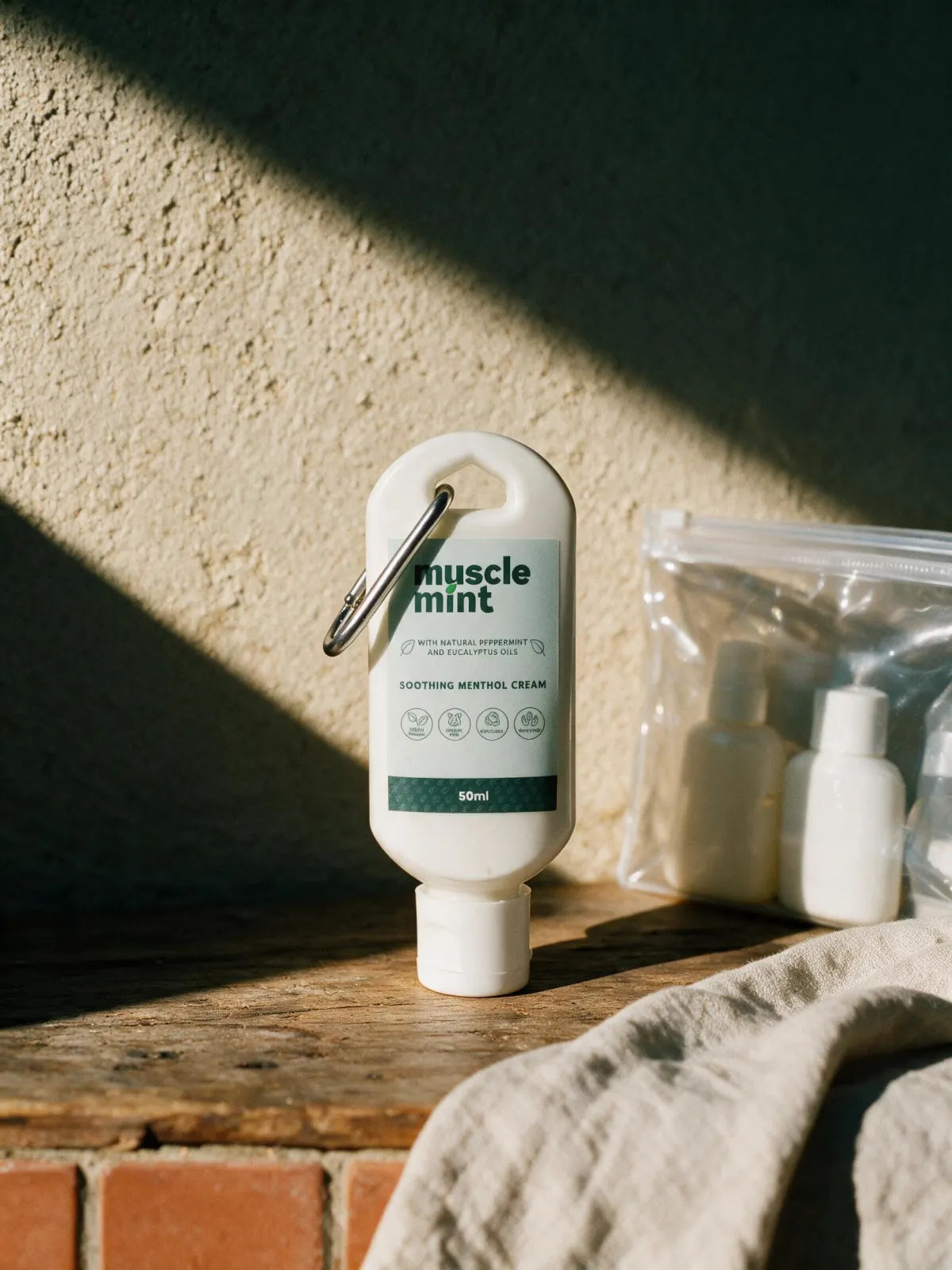 Muscle Mint 50 ml Travel bottle standing beside a packed clear liquids bag against a plaster wall