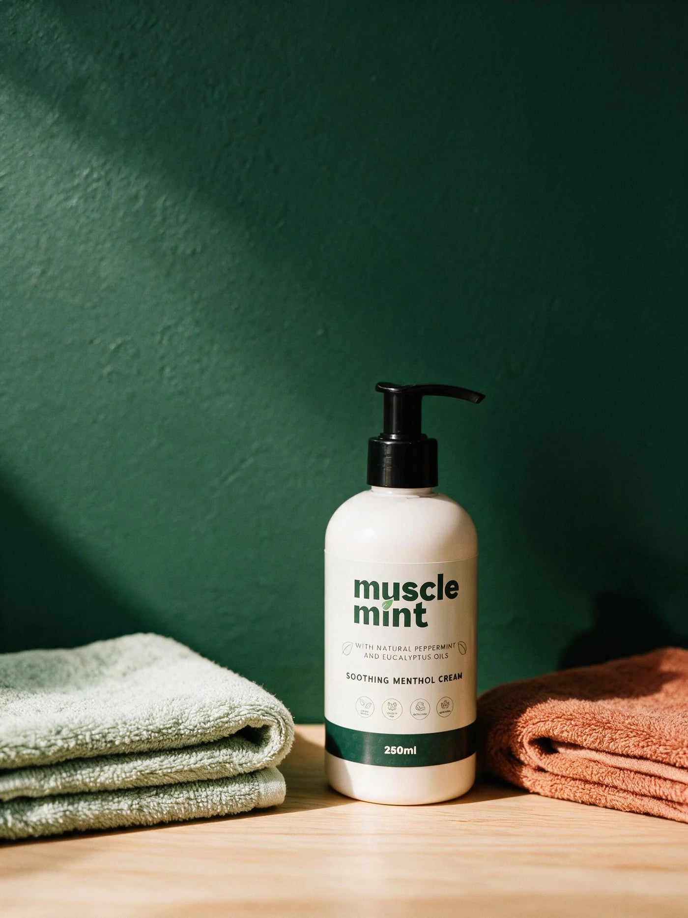 Muscle Mint 250ml bottle between a folded sage towel and a folded terracotta towel