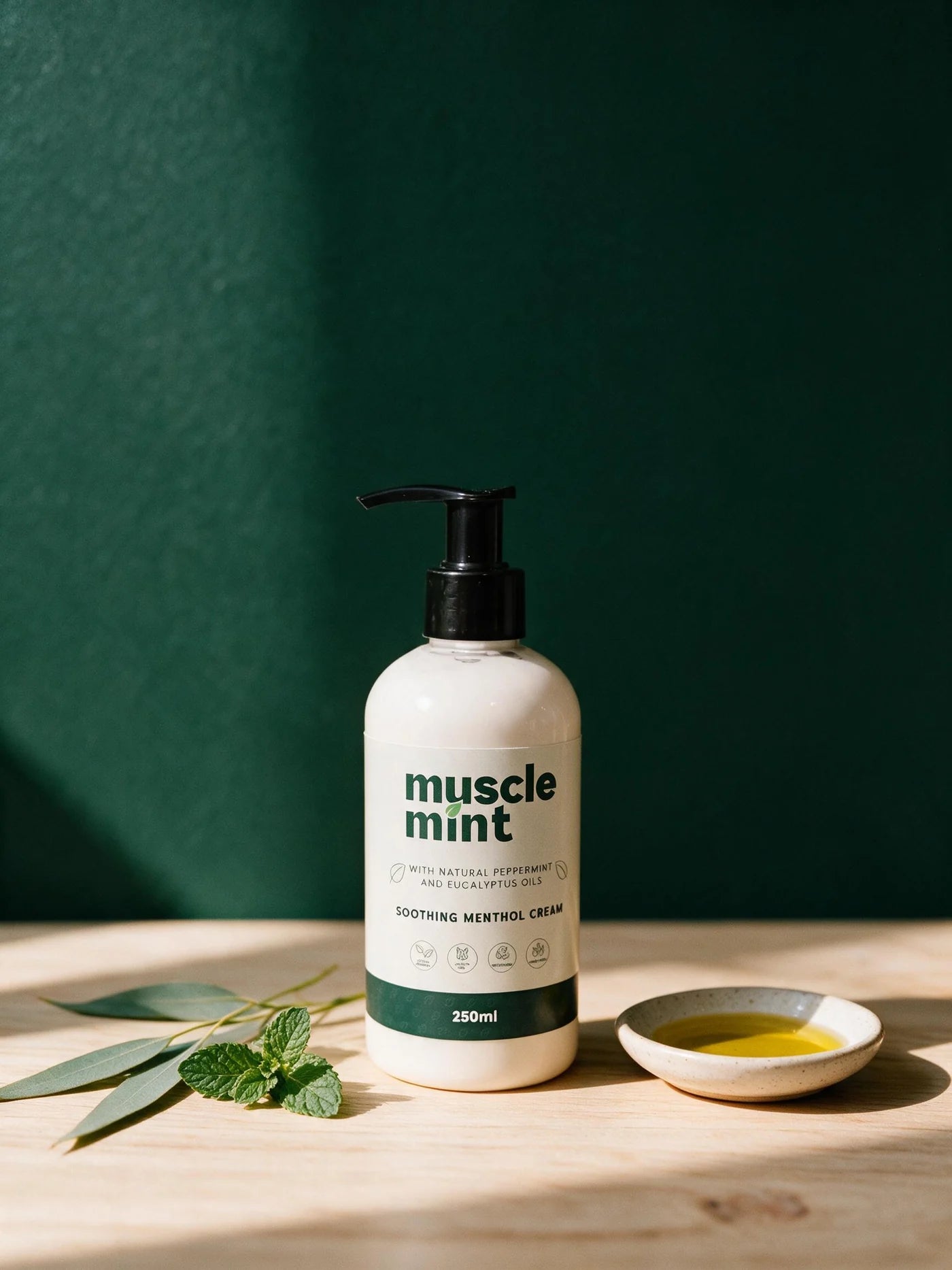 Muscle Mint 250ml bottle beside fresh peppermint, eucalyptus leaves and a dish of sunflower oil