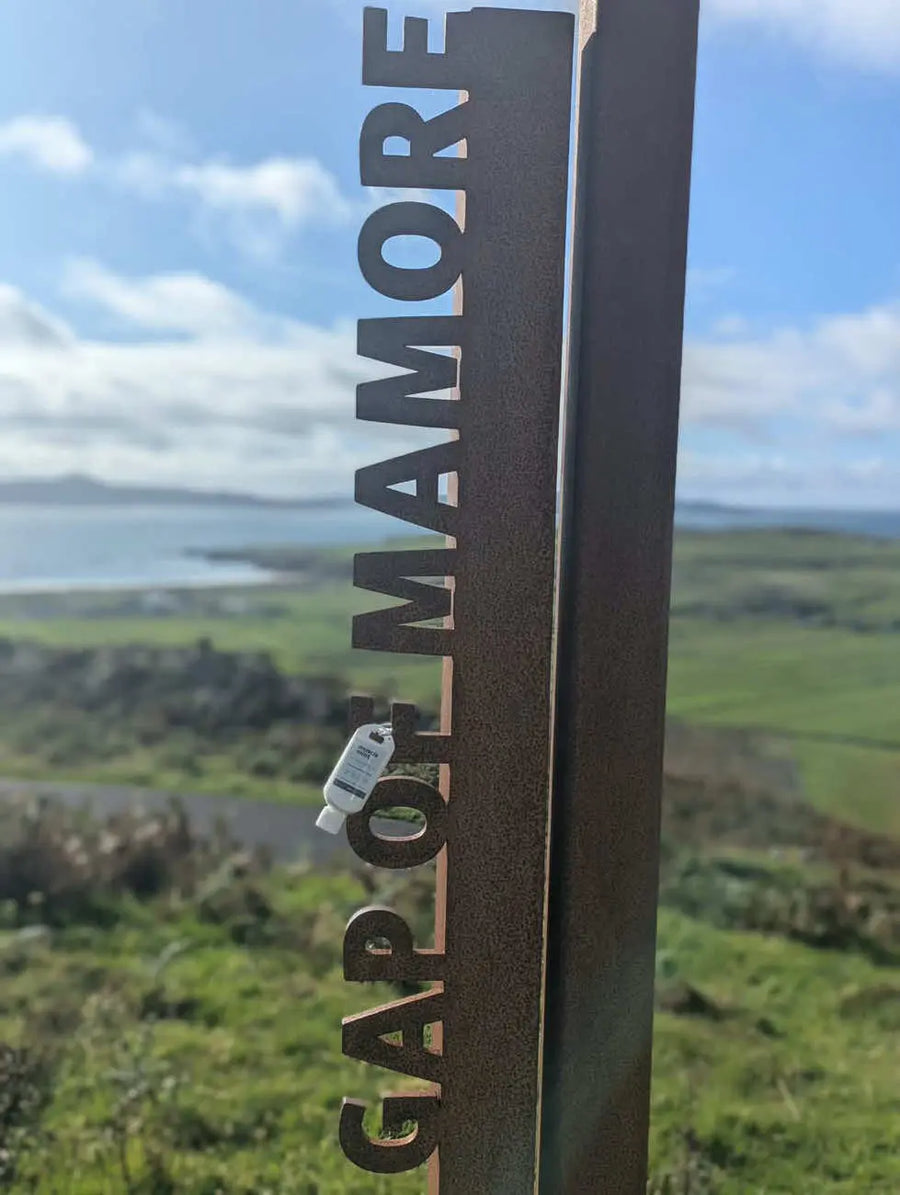 Muscle Mint 50ml travel size menthol cream clipped into the letter O of the metal Gap of Mamore sign, green hills and the Atlantic coast behind