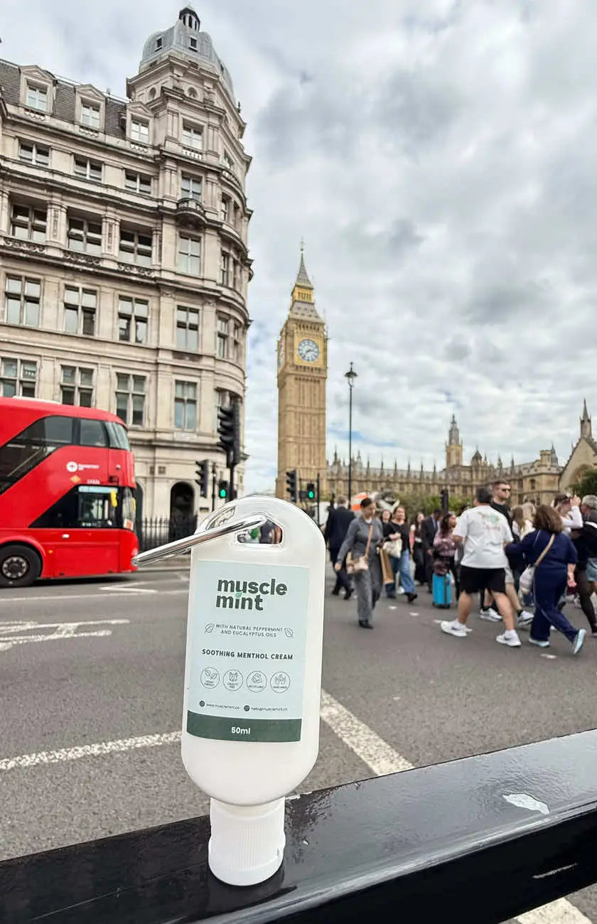 Muscle Mint 50ml travel size menthol cream on a black railing with Big Ben, the Houses of Parliament and a red London bus behind